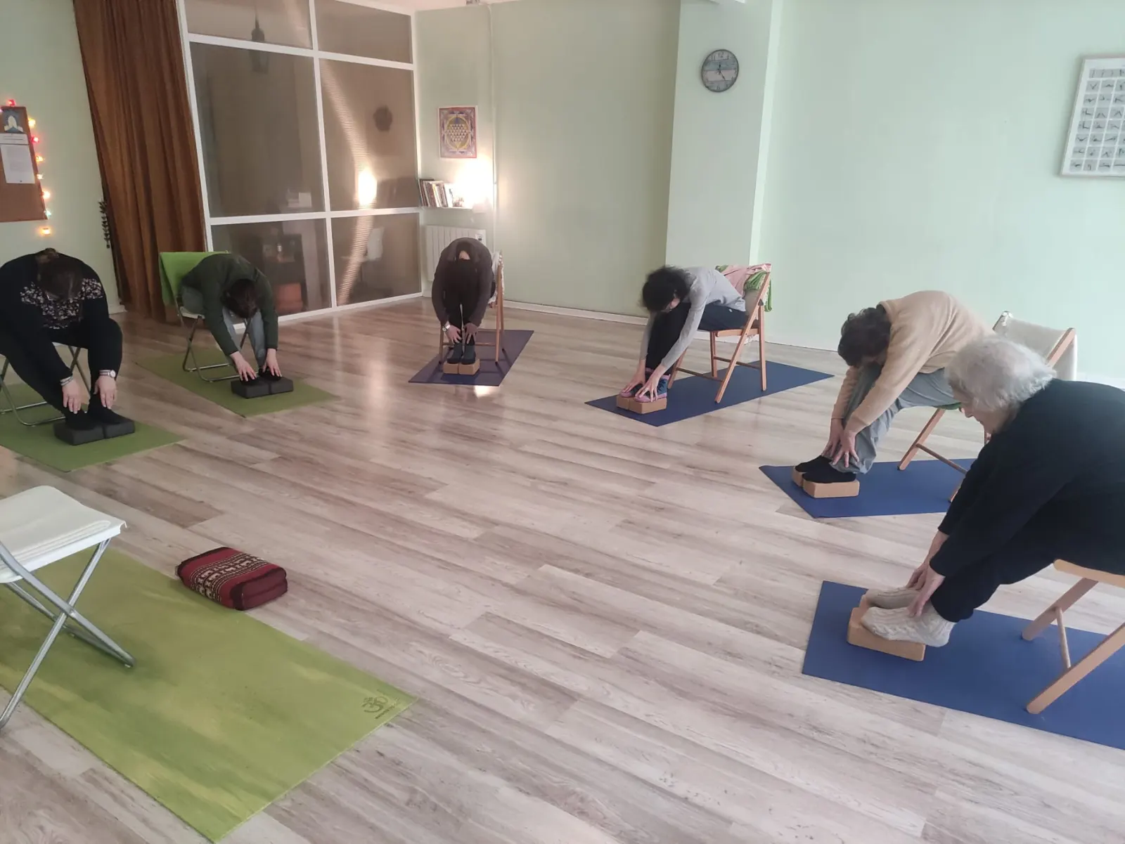 Grupo practicando yoga con sillas y bloques en la sala