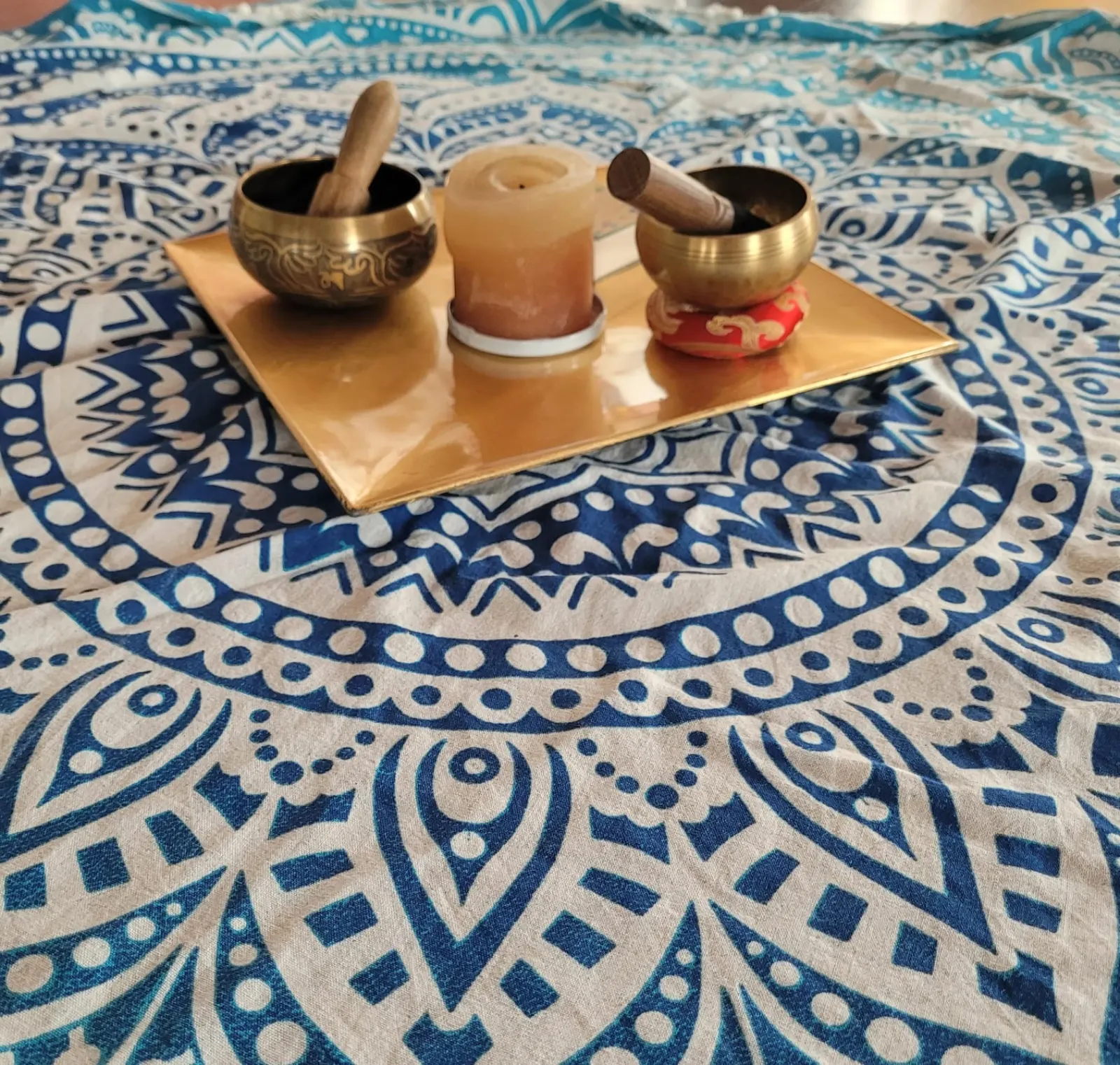 Dos cuencos tibetanos y una vela sobre una bandeja dorada, encima de un tapiz de mandala azul
